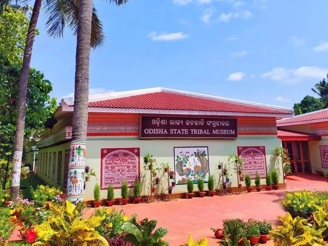 Odisha State Tribal Museum Bhubaneswar main building red roof Pattachitra murals palms yellow flowers entrance, perfect Odisha tribal heritage culture tour package. 