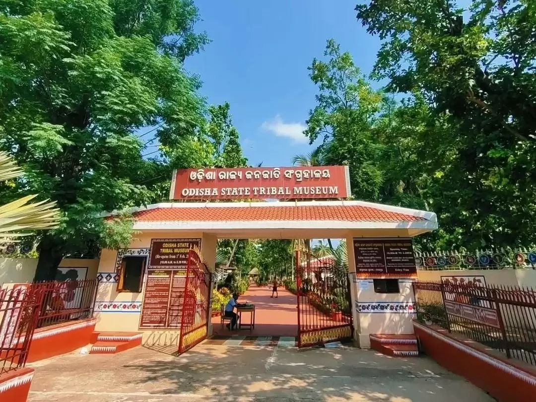Odisha State Tribal Museum Bhubaneswar grand red entrance gate Odisha script trees lush greenery pathway, perfect Odisha tribal heritage culture tour package. 
