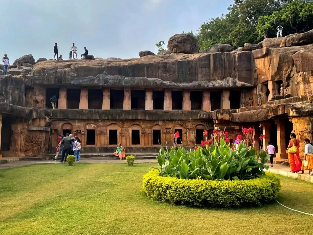Udayagiri Caves Odisha tourists exploring double-tier rock-cut facade landscaped garden red canna lilies hilltop views, perfect Bhubaneswar Jain heritage tour package.