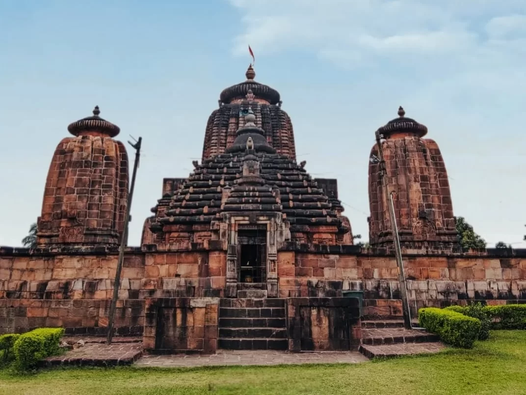 Brahmeswara Temple at Bhubaneswar on clear day, featuring three Kalinga spires and Odisha flag, perfect heritage Bhubaneswar tour package.