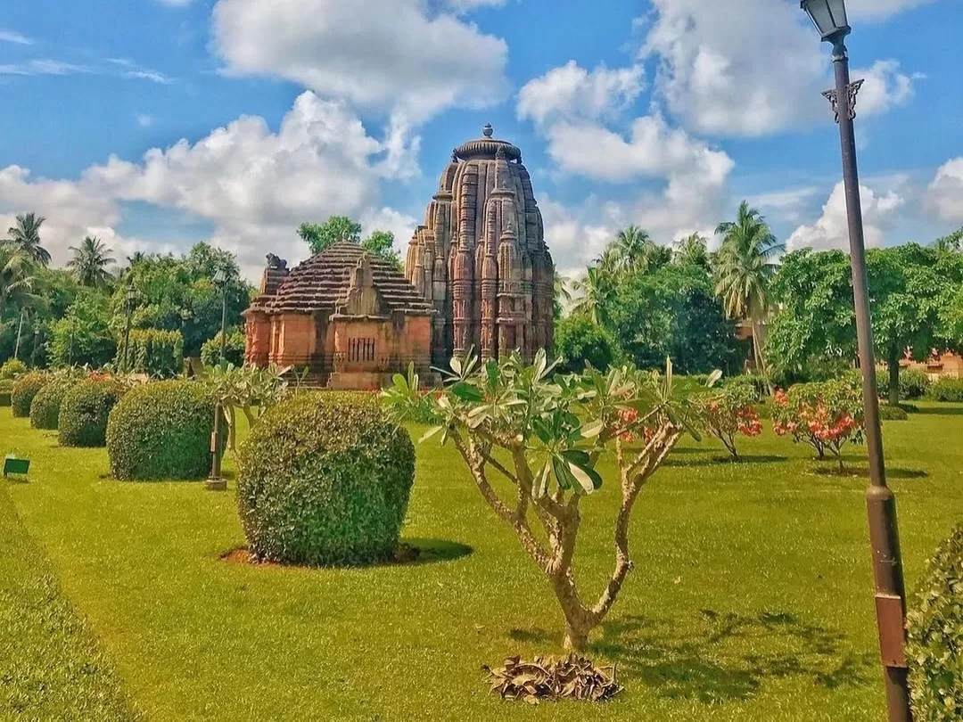 Rajarani Temple Bhubaneswar 11th century Kalinga architecture red sandstone vimana landscaped garden palms streetlamp blue sky, perfect Odisha heritage tour package.
