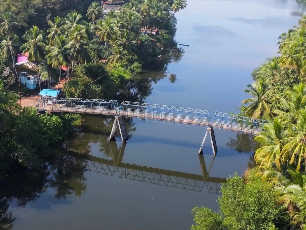 Aerial view of Zuem Bridge over river at Majuli Assam during clear day, featuring coconut palms, huts and reflections, perfect adventure experience Majuli tour package.