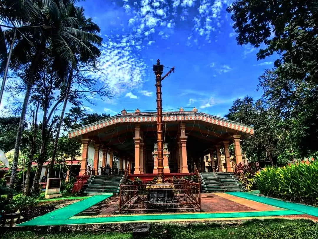 Iconic Tirupati Balaji Temple North Goa under blue skies with prominent flagpole and ornate architecture, surrounded by palms and vibrant gardens, perfect faith-filled visit with Goa tour package.
