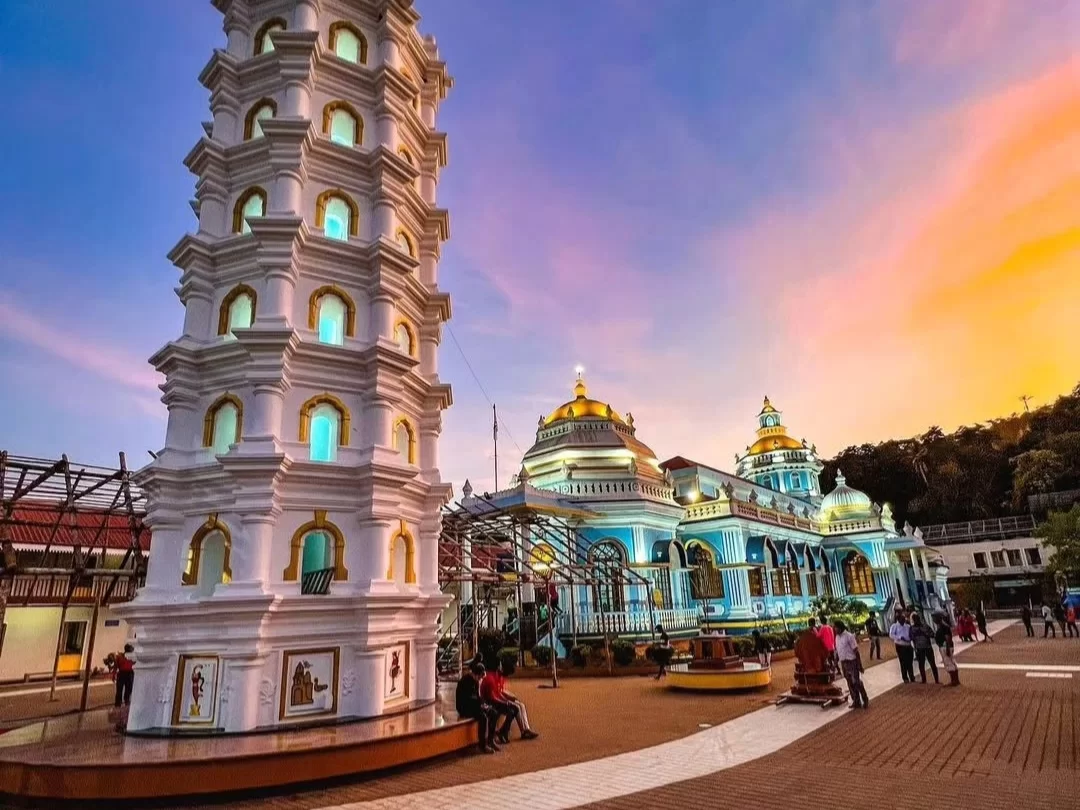 Devotees at Shree Mangesh Temple in Goa during sunset twilight, featuring illuminated white tower, blue domes and golden sky, perfect spiritual experience with Goa tour package. 