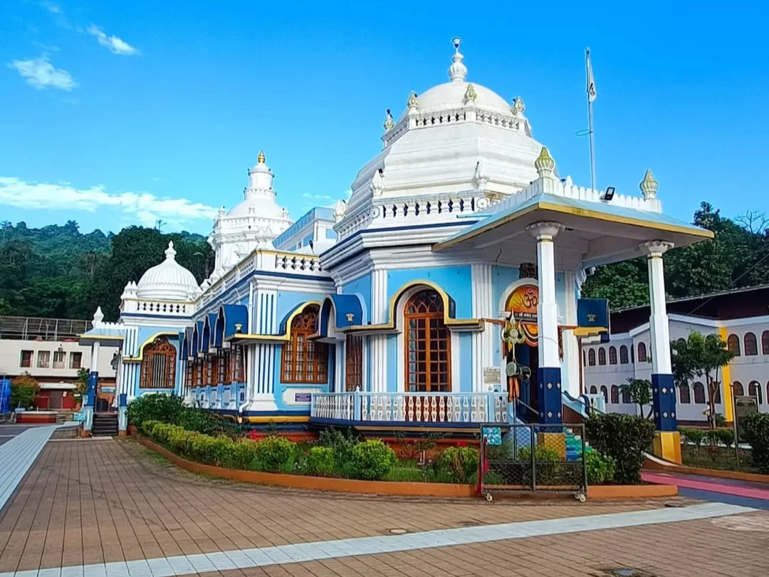 Shree Mangesh Temple facade in Goa during blue skies, featuring white domes, blue arches, golden kalash and leafy hills, perfect spiritual experience with Goa tour package.