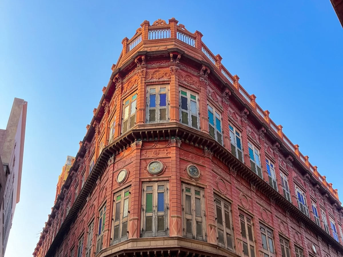 Rampuriya Haveli Bikaner Rajasthan corner view, featuring ornate red sandstone building multicolored windows intricate carvings blue sky, perfect Rajasthan tour packages.