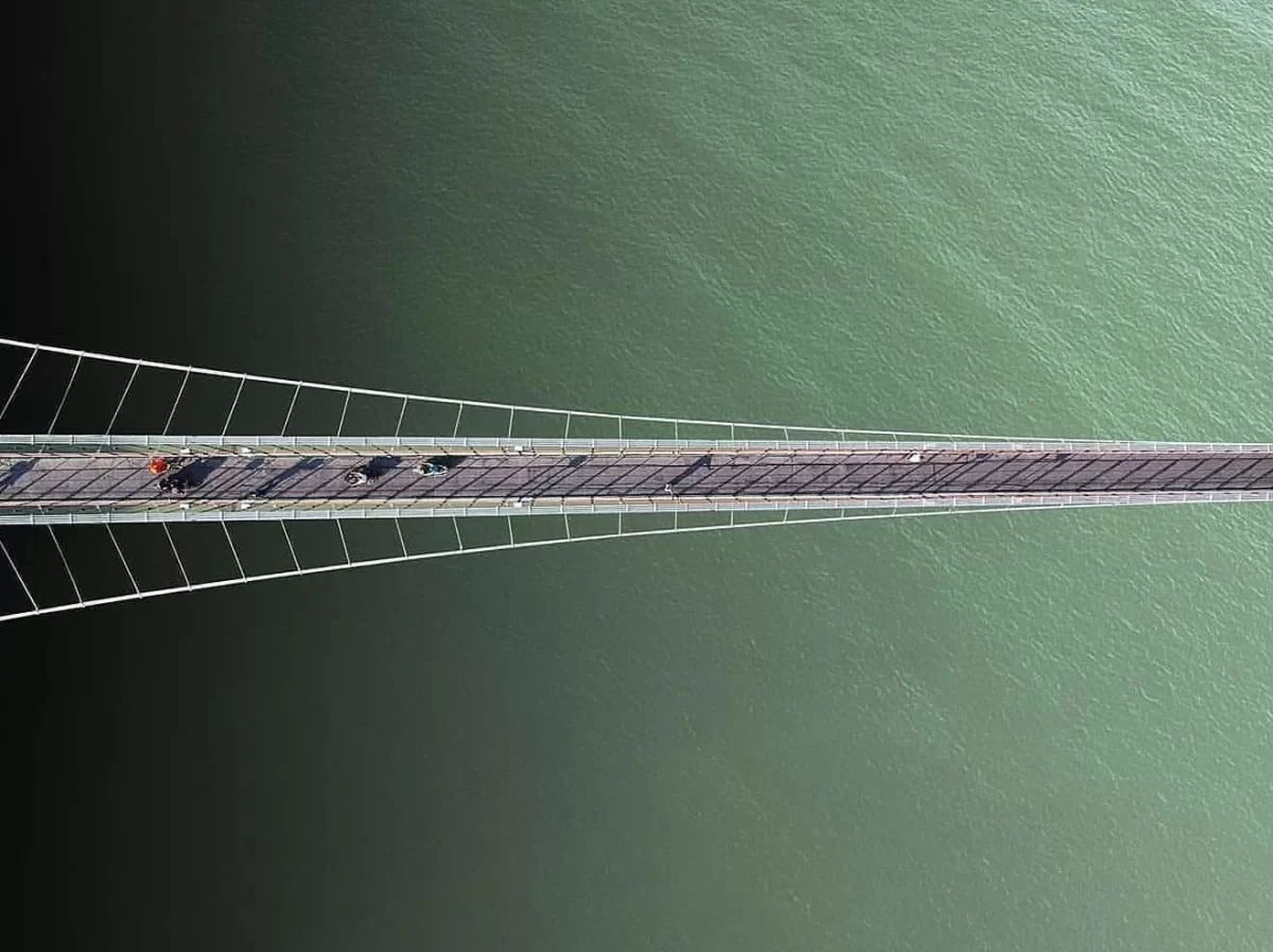 Laxman Jhula suspension bridge at Rishikesh over Ganga River, aerial view featuring cable structure turquoise water walkers, perfect spiritual experience Uttarakhand tour package.