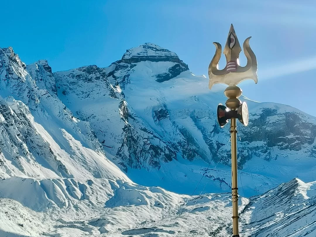 Golden Trishul at Adi Kailash during sunny day, featuring snow-capped peaks and blue sky, perfect spiritual Uttarakhand tour package.