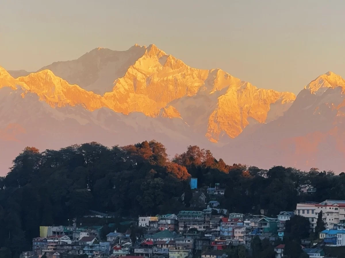 Golden sunrise on Kanchenjunga from Tiger Hill in Darjeeling, featuring glowing snow peaks above hillside town, perfect Sikkim tour package