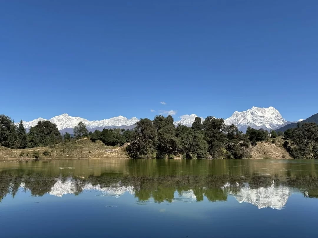 Deoria Tal Lake mirror reflection of Chaukhamba peaks with forest and blue sky near Chopta in Uttarakhand tour packages.