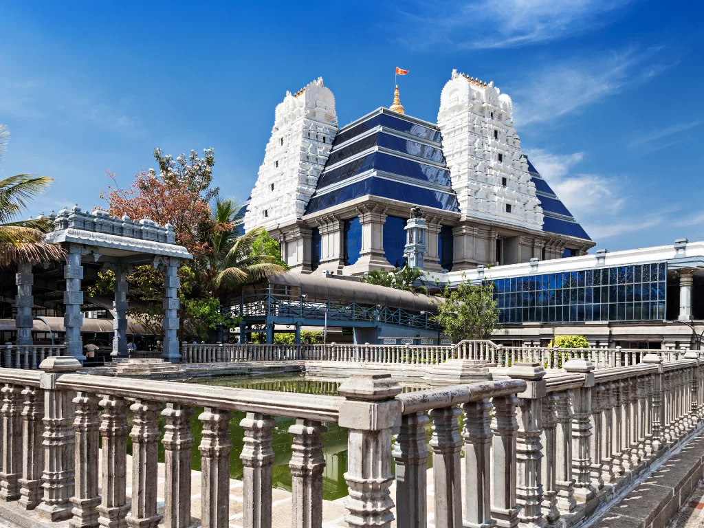 ISKCON Temple Bangalore clear sky, tiered white gopurams blue glass flag palms trees pillars canopy pond, perfect Karnataka tour package.