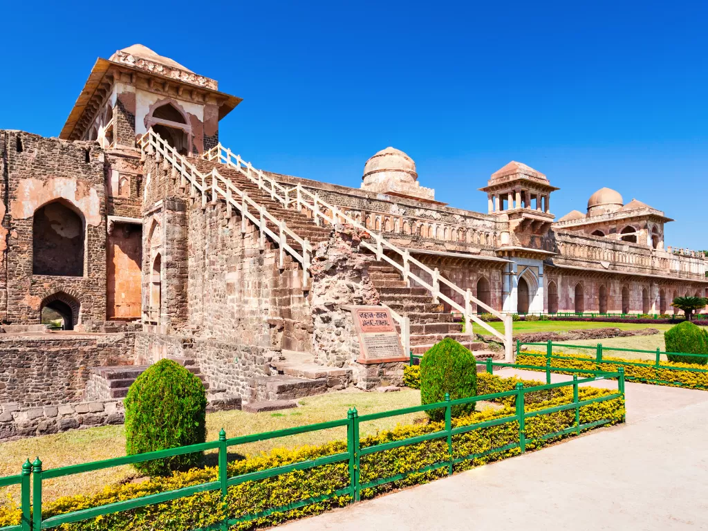Jahaz Mahal at Mandu under clear skies, featuring grand front staircase with signboard and multiple domes amid gardens, perfect heritage experience with Madhya Pradesh tour packages.