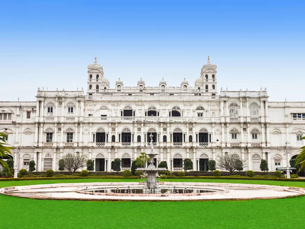 Jai Vilas Palace Gwalior during clear afternoon, featuring white Italianate facade with Tuscan-Doric-Corinthian architecture, central crystal fountain, and manicured gardens with palms, perfect heritage experience in Madhya Pradesh tour package.