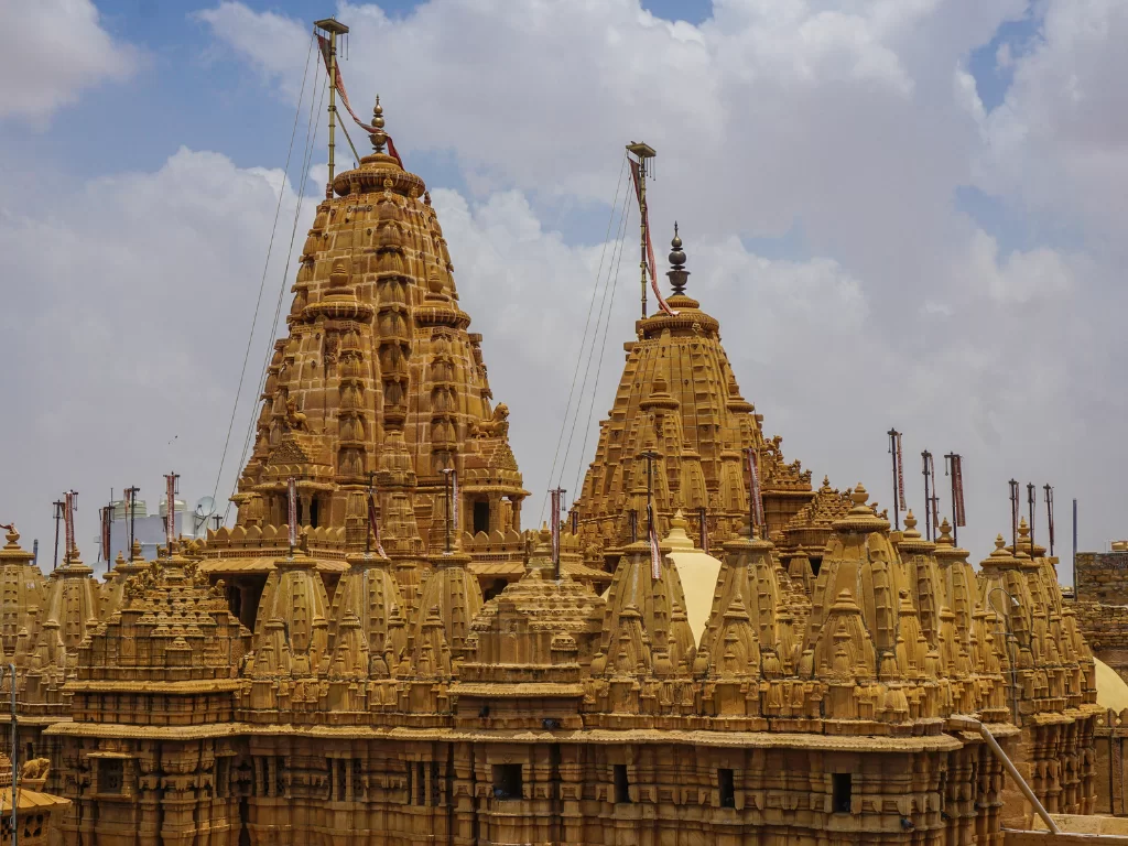 Towering shikharas at Jain temple Jaisalmer during partly cloudy day, featuring intricate carvings & domes, perfect romantic experience Rajasthan tour packages. 
