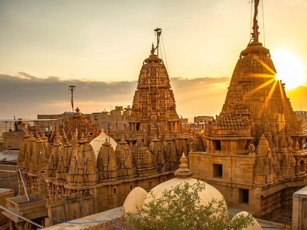 Golden Jain temples cluster at Jaisalmer during sunset glow, featuring intricate shikharas & domes, perfect romantic experience Rajasthan tour packages.
