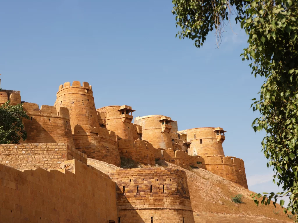 Golden sandstone towers at Jaisalmer Fort during sunny day, featuring bastions & trees, perfect adventure experience Rajasthan tour packages.
