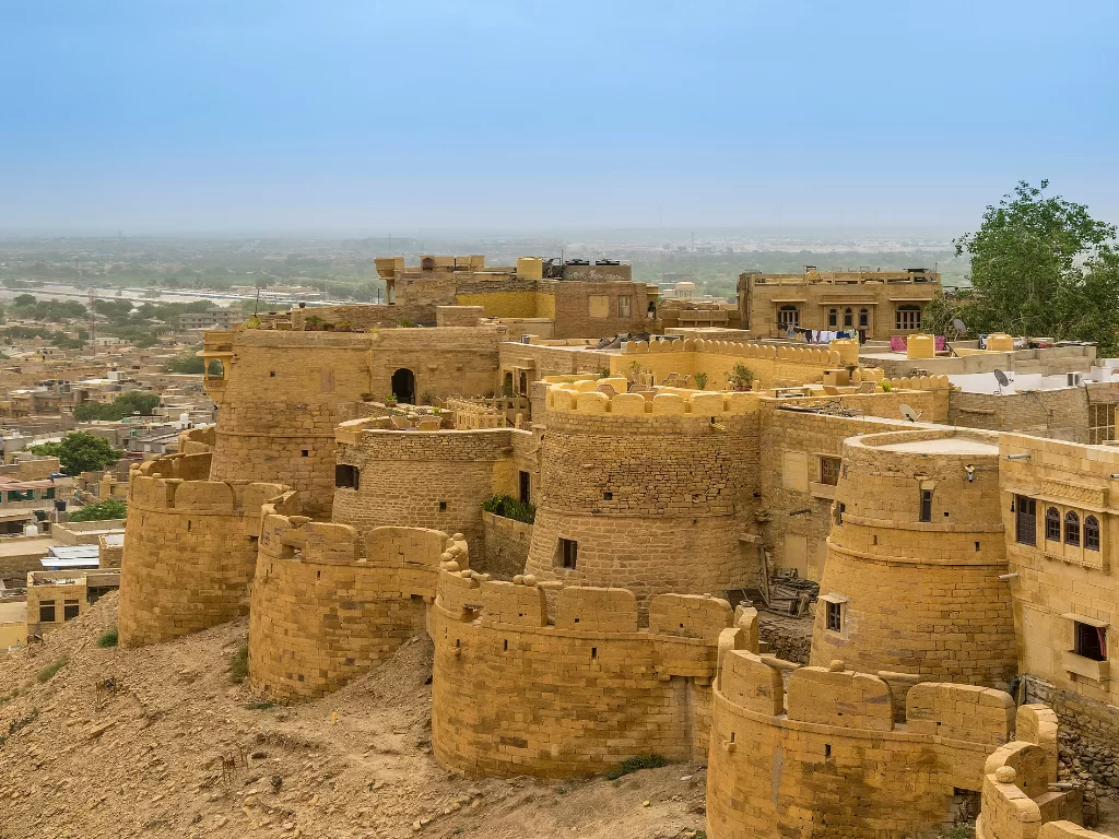 Curved bastions at Jaisalmer Fort during clear sky, featuring golden towers & cityscape, perfect adventure experience Rajasthan tour packages. 