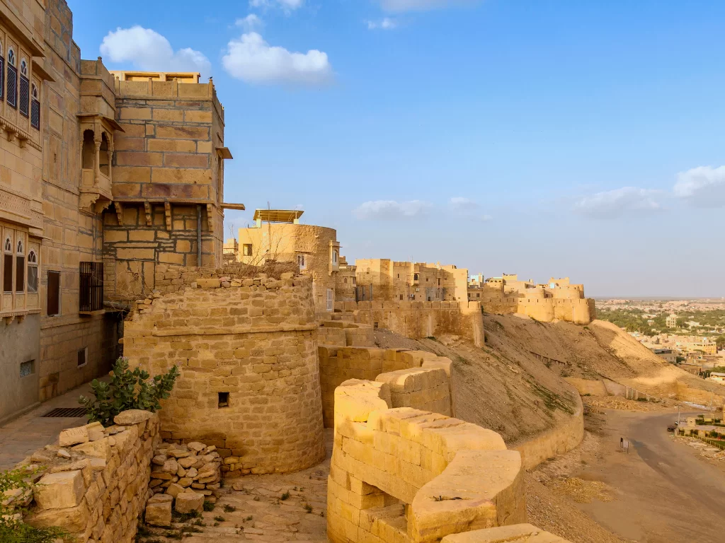 Sandstone ramparts at Jaisalmer Fort during sunny day, featuring turrets & distant skyline, perfect adventure experience Rajasthan tour packages. 