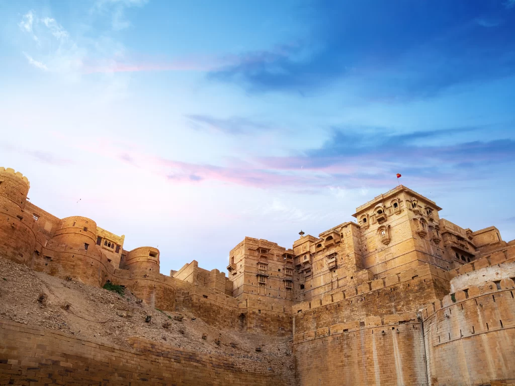 Towering walls at Jaisalmer Fort during sunset glow, featuring pink hues & ramparts, perfect romantic experience Rajasthan tour packages.