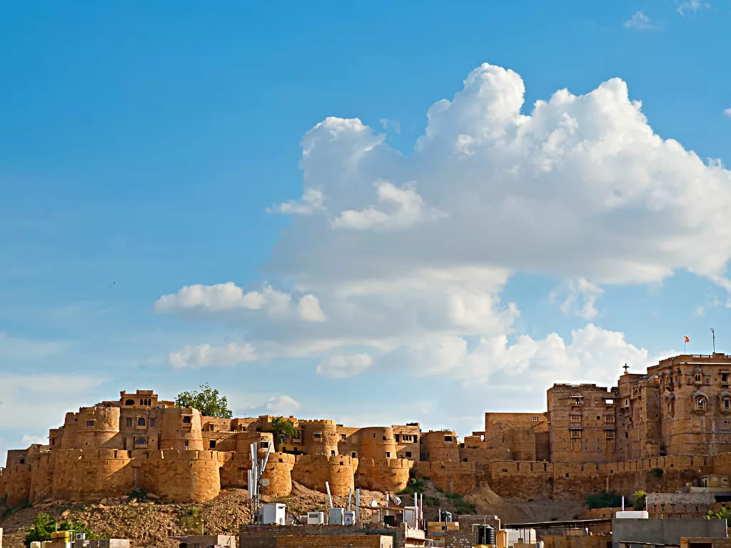 Golden ramparts at Jaisalmer Fort during partly cloudy sky, featuring bastions & desert hills, perfect adventure experience Rajasthan tour packages.
