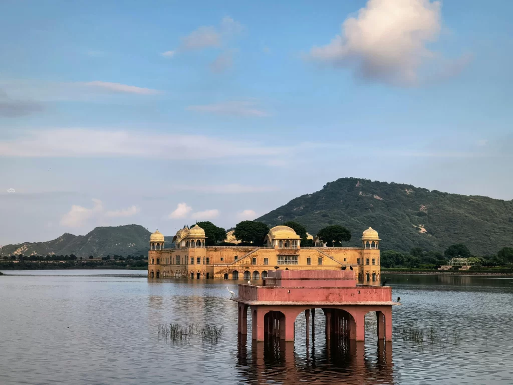 Jal Mahal palace at Jaipur under partly cloudy sky, featuring pink pavilion reed lake Aravalli hills, perfect romantic experience Rajasthan tour packages.