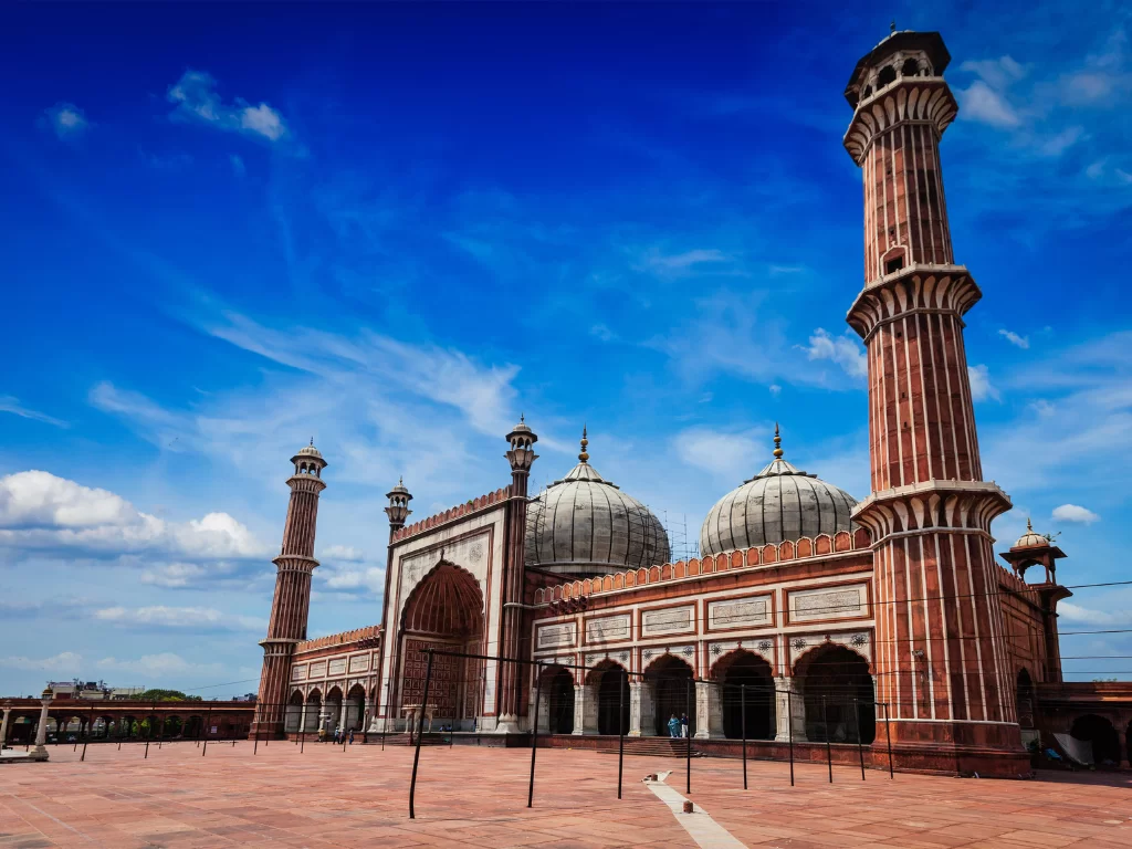 Jama Masjid Delhi front view with domes and minarets under blue sky, iconic Mughal mosque and major tourist attraction in Old Delhi tour packages