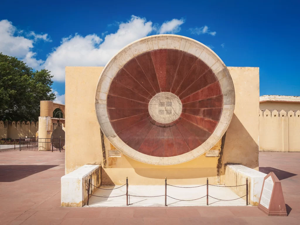 Chakra Yantra at Jantar Mantar Jaipur during clear day, featuring large stone dial and architectural walls, perfect heritage experience Rajasthan tour packages.