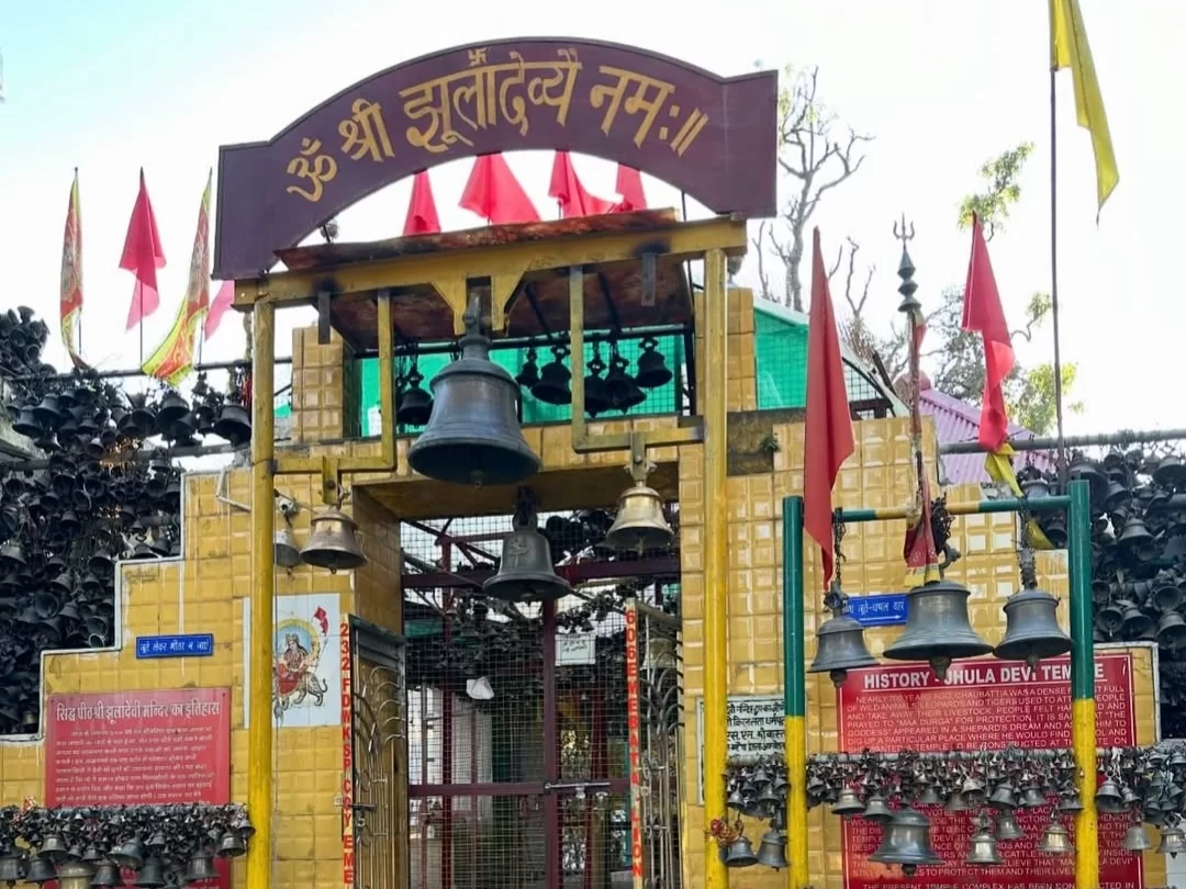 Entrance of Jhula Devi Temple in Ranikhet, Uttarakhand adorned with numerous hanging bells and red flags, a revered shrine included in Uttarakhand tour packages