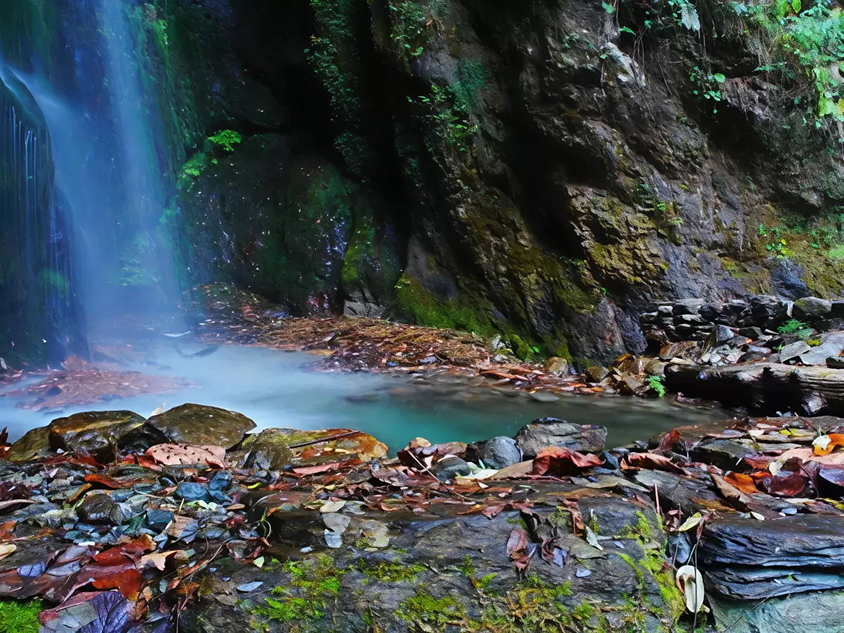 Jibhi Waterfall Tirthan Valley Himachal Pradesh during misty conditions, featuring cascading falls turquoise pool mossy boulders dense green forested rocky gorge backdrop, perfect cultural experience Himachal tour package.