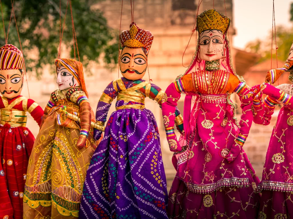 Colorful Rajasthani puppets at Jodhpur's Blue Corridor during sunset, featuring traditional attire and temple backdrop, perfect cultural experience in Rajasthan tour package.
