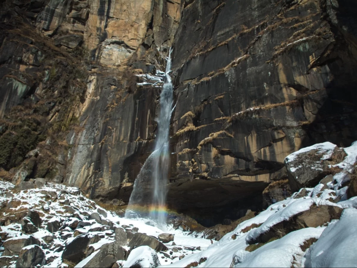 Jogini Waterfall Manali Winter majestic view, featuring cascading falls rocky cliffs snowy base rainbow mist, perfect Himachal Pradesh trekking tour package.