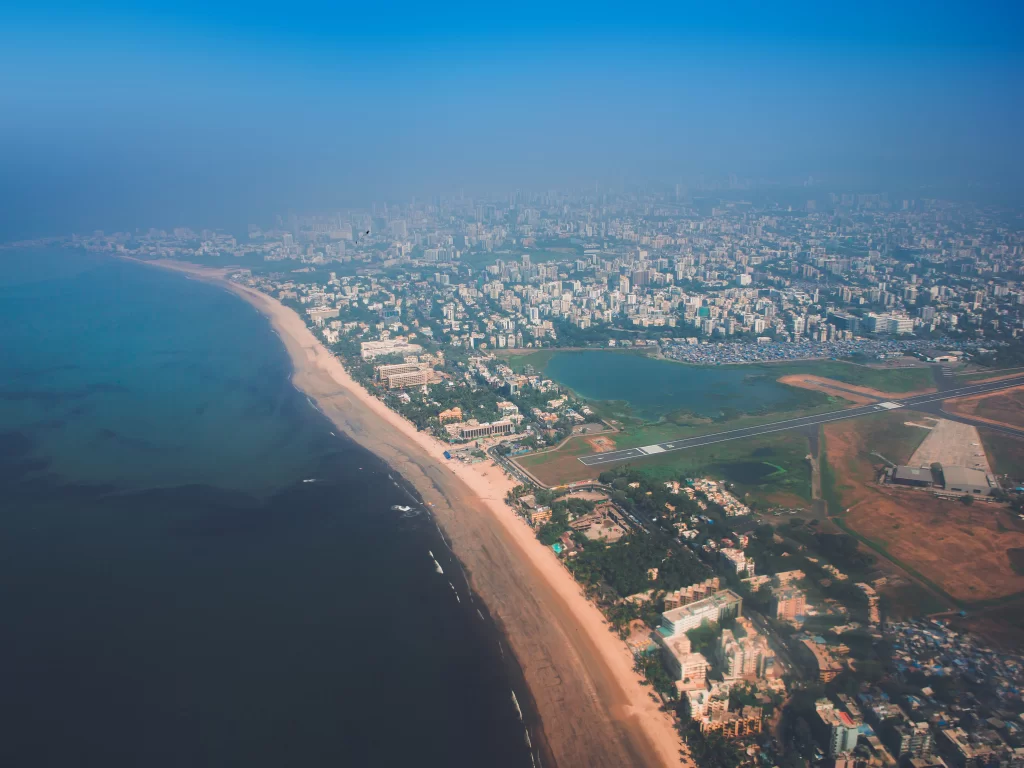 Aerial view of Juhu Beach Mumbai during hazy afternoon, featuring sandy shores, Arabian Sea waves, and Chhatrapati Shivaji Airport runway, perfect beach experience for Mumbai tour package. 