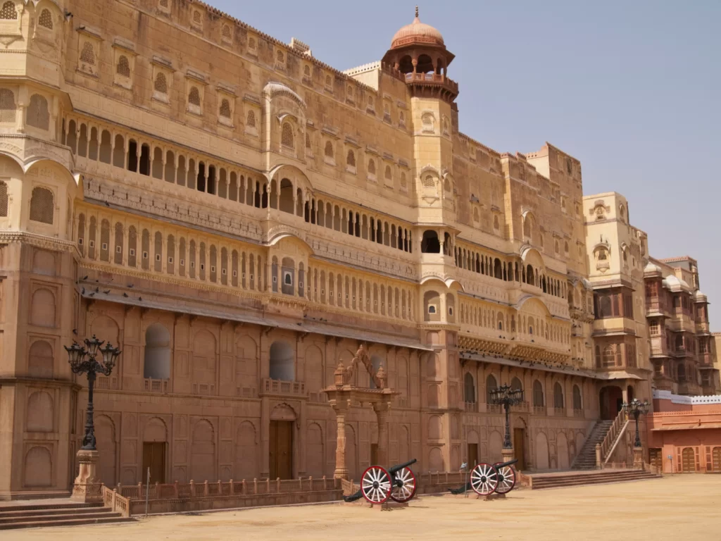 Sunlit courtyard of Junaghar Fort in Bikaner at midday, featuring grand facade and cannons, perfect Bikaner heritage tour package