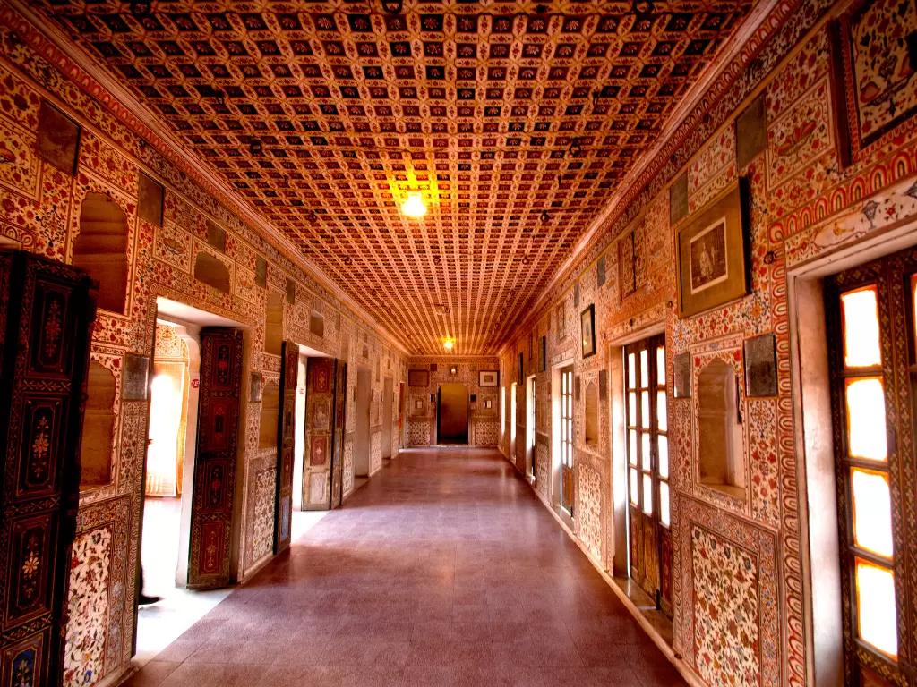 Ornate corridor inside Junaghar Fort in Bikaner during daytime, featuring painted walls and carved doors, perfect Bikaner heritage.