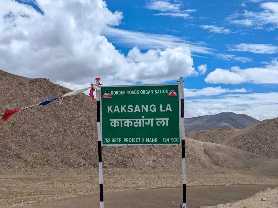 BRO signboard at Kaksang La pass during partly cloudy skies, featuring prayer flags, barren Himachal mountains, perfect high-altitude adventure Ladakh tour package.