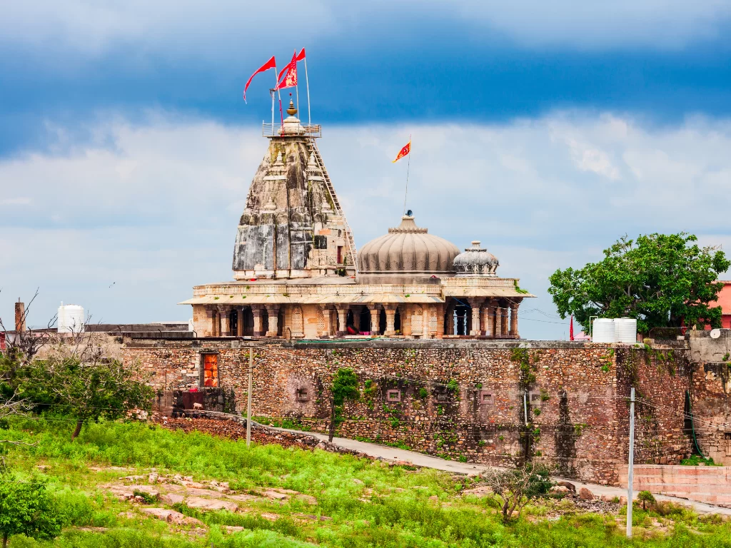 Kalika Mata Temple on Chittorgarh Fort wall in Rajasthan under partly cloudy sky, featuring saffron flags and stone ramparts, perfect Rajasthan tour package