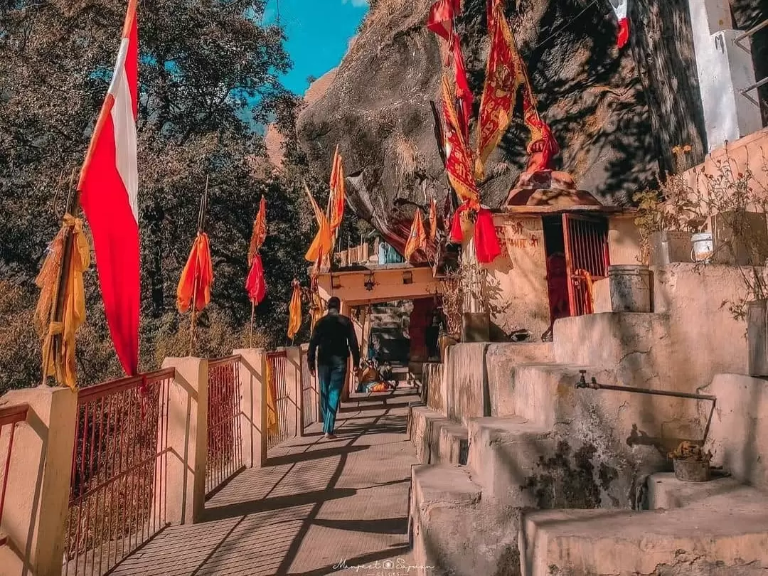 Kalpeshwar Temple entrance pathway in Uttarakhand with colorful flags and scenic mountain surroundings, sacred pilgrimage spot featured in Uttarakhand tour packages