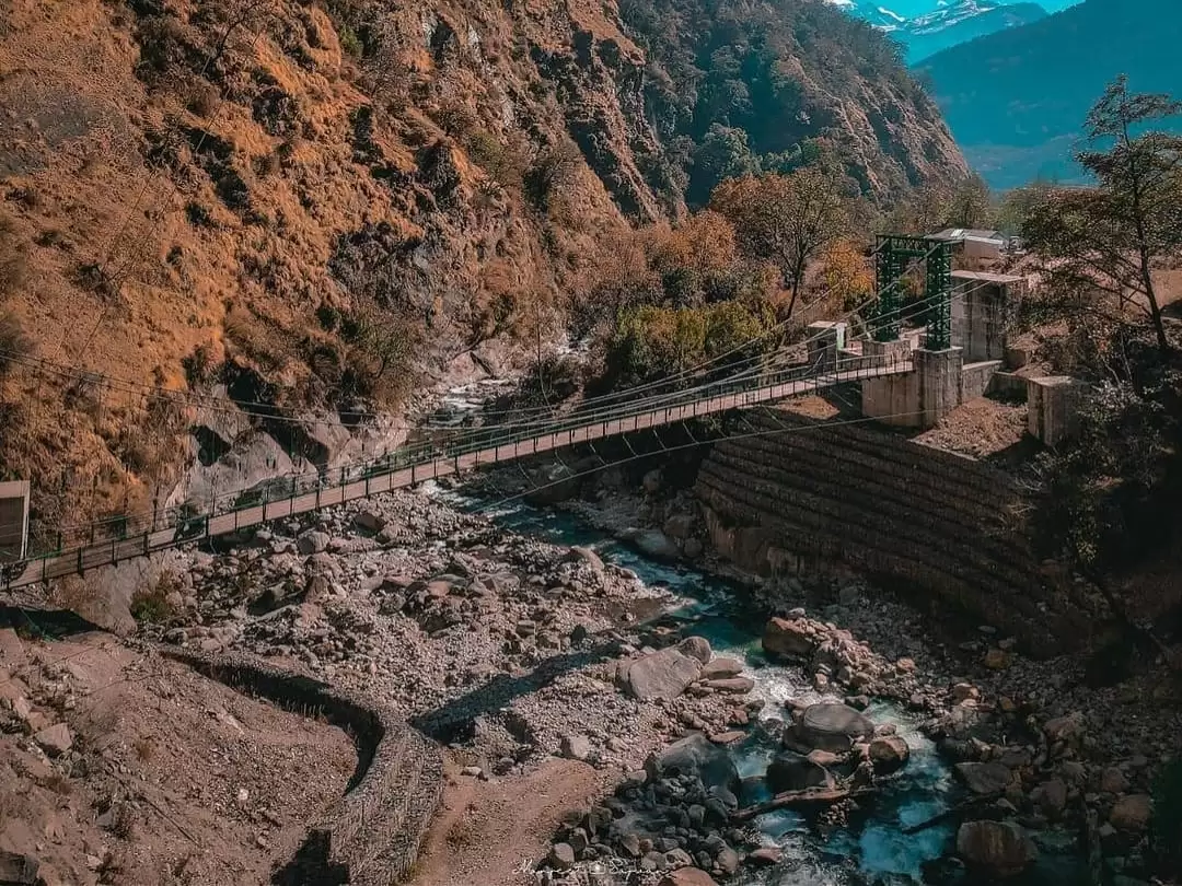 Suspension bridge over rocky river near Kalpeshwar Mahadev in Urgam Valley, Uttarakhand, surrounded by scenic mountains and peaceful landscapes featured in Uttarakhand tour packages