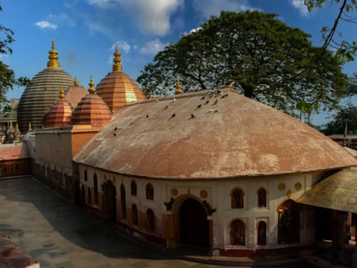 Kamakhya Temple Guwahati complex on Nilachal Hill during clear afternoon, featuring rustic domes, courtyard and tree canopy, perfect spiritual experience Assam tour package.