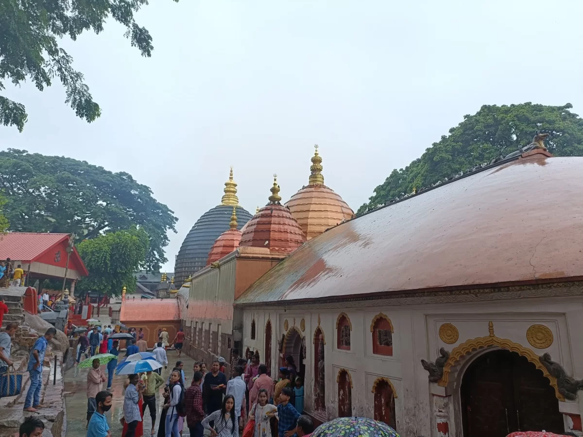 Pilgrims at Kamakhya Temple Guwahati during light rain, featuring Nilachal-style domes, trees and umbrellas, perfect spiritual experience Assam tour package.