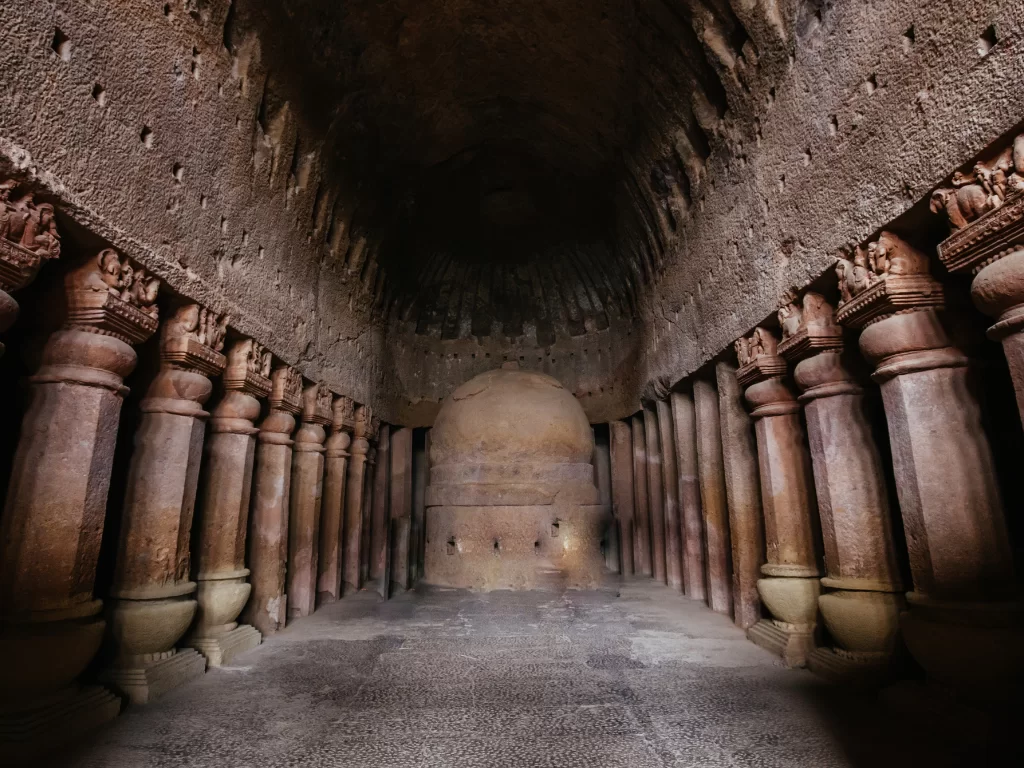 Cave interior at Kanheri Caves Mumbai Maharashtra during dim light, featuring stupa, carved pillars, vaulted ceiling, perfect heritage experience Mumbai tour package. 