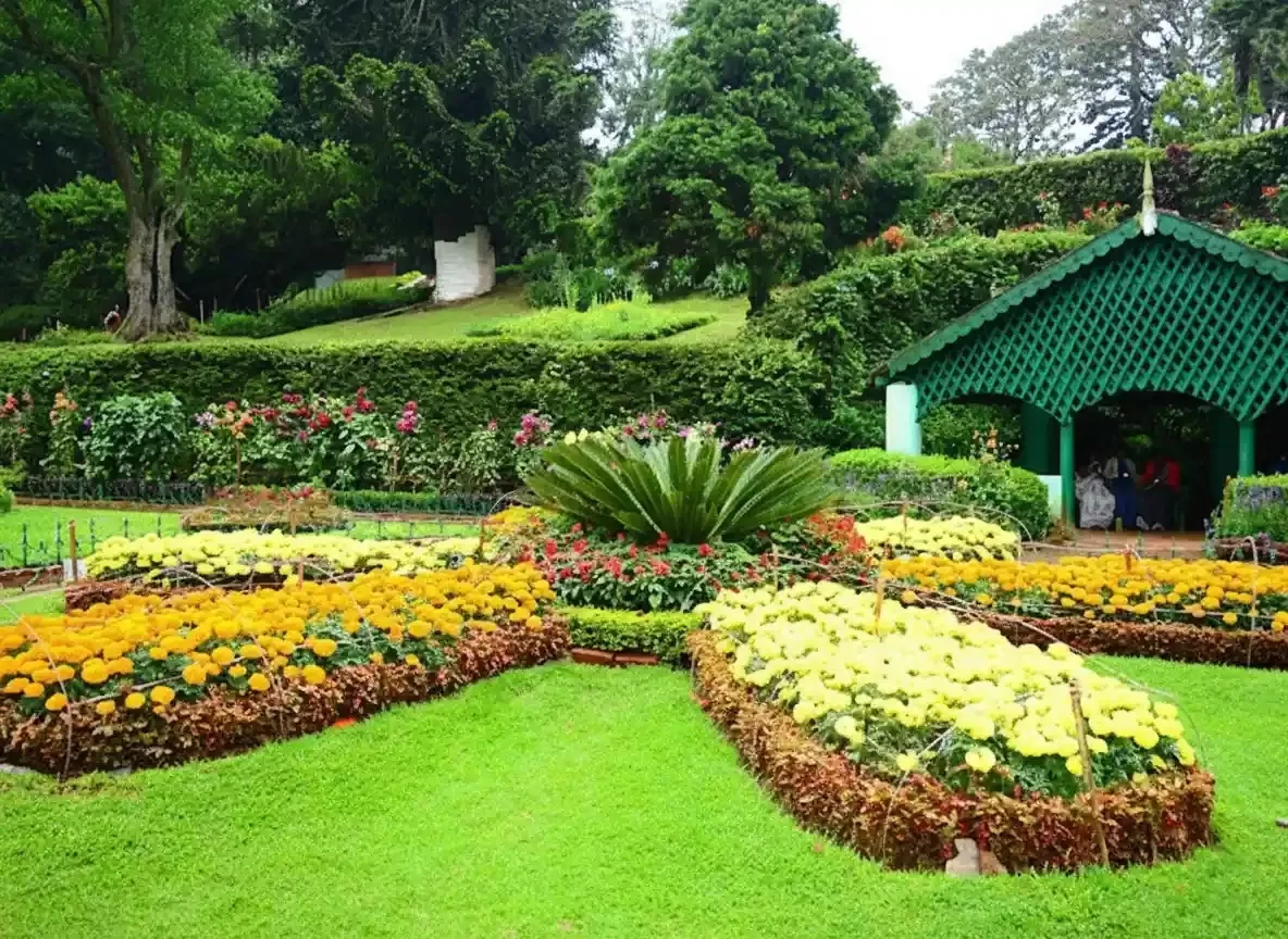 Kattery Park in Coonoor featuring lush terraced gardens, colorful flower beds, and the scenic Kattery Falls in the background.