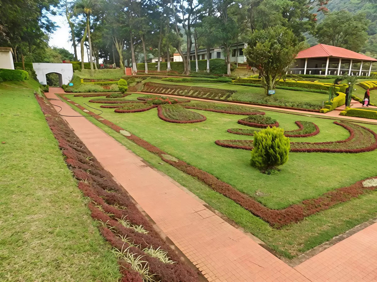 Kattery Park Coonoor landscaped garden during sunny day, featuring artistic flower beds, pathways and Nilgiri trees, perfect Tamil Nadu tour package.