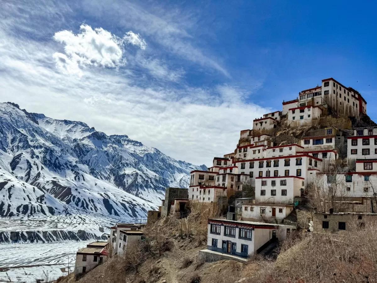 Kaza Monastery Spiti Valley winter panoramic, featuring multi-tiered white red-roofed gompa perched hillside snowy Himalayan peaks blue skies clouds, perfect Himachal Pradesh tour packages.