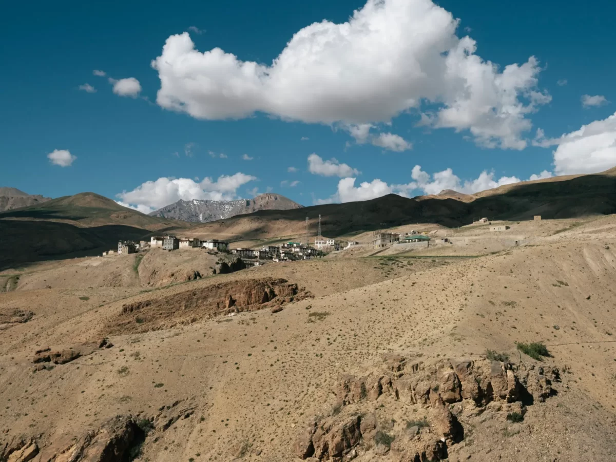 Kibber Village near Kaza during partly cloudy skies, featuring traditional houses rocky terrain brown hills snow mountains, perfect cultural experience Himachal tour package.