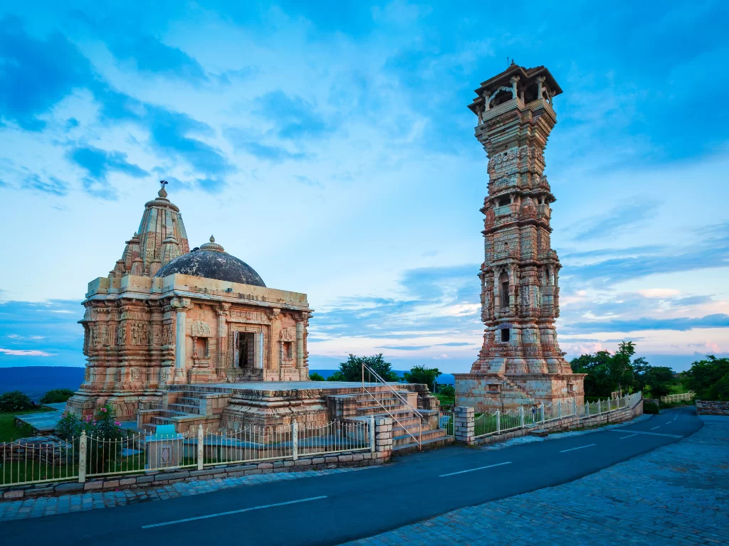 Kirti Stambh tower beside temple at Chittorgarh Fort in Rajasthan at twilight, featuring shikhara dome and railing, perfect Rajasthan tour package.