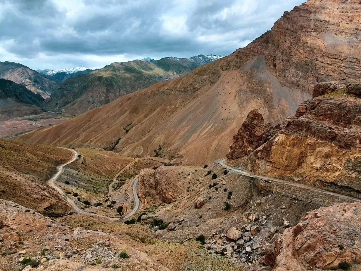 Spiti Valley road near Komic Village Kaza during cloudy skies, featuring winding highway brown rocky cliffs snow mountains, perfect adventure experience Himachal tour package.