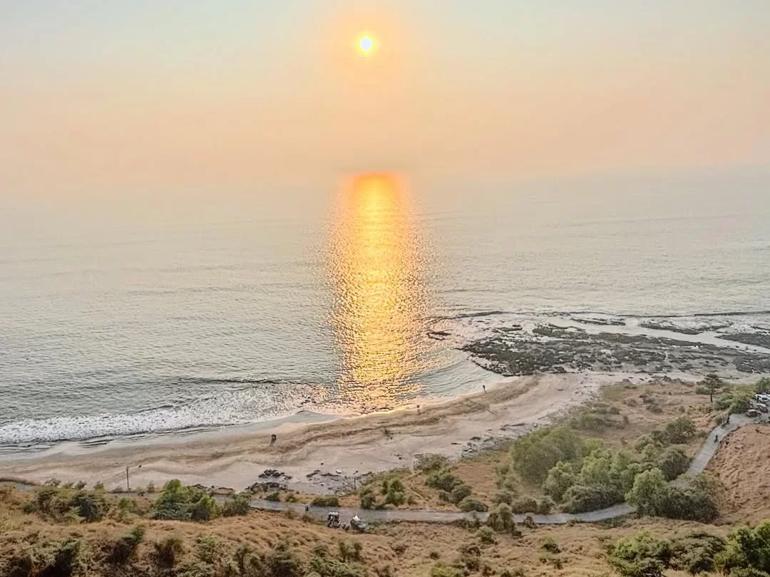 Sunset view over Korlai Beach in Maharashtra, with golden reflections on the Arabian Sea and a quiet shoreline below the hillside, a scenic coastal stop included in Maharashtra tour packages.