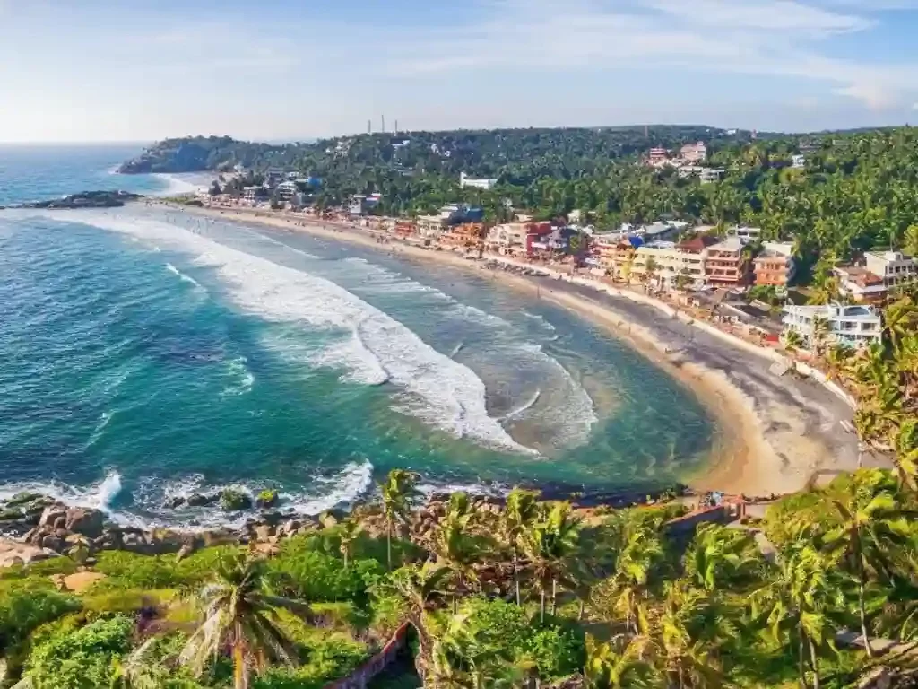 Kovalam Beach in Chennai featuring the crescent shoreline, surfers on blue waves, and the iconic lighthouse on the rocks.