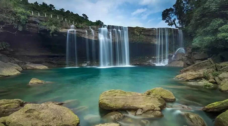 Krang Shuri Falls in Meghalaya, crystal clear turquoise pool beneath cascading waterfall cliffs.